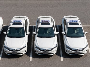 Overhead view of three rideshare sedans parked in formation in a fleet yard, even natural daylight, vehicle rooftops clearly visible with Uber signage, clean asphalt surface