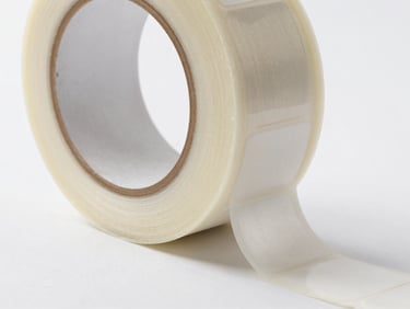 Close-up of a freshly printed BOPP tape roll edge and a sheet of die-cut labels on a release liner under bright studio lighting, sharp print registration detail visible, no people