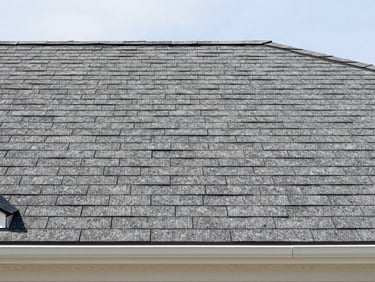 Straight-on medium shot of clean residential roofline with newly replaced shingles, bright daylight