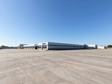 Wide-angle photograph of a clean, flat commercial land plot in Imbituva, bright natural daylight, clear blue sky, professional real estate perspective