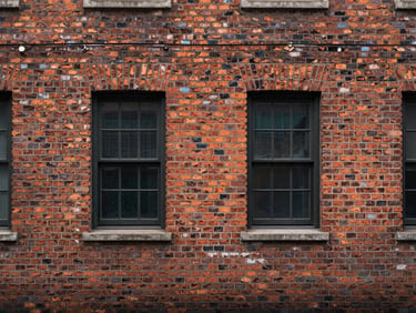 Straight-on elevation study of a brick facade — bond pattern, weathering, and window reveals under flat overcast light, no people or foreground obstruction