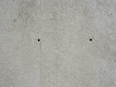 Close macro shot of raw concrete surface under north-facing daylight — aggregate texture, formwork tie holes, honest patina with no shadow ambiguity
