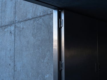 A dramatic, low-key architectural close-up of a massive reinforced concrete wall meeting a heavy brushed steel vault door frame, deep shadows, cool midnight blue highlights, geometric composition.