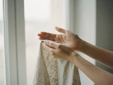Hands holding raw linen fabric under soft window light, detailed texture, minimalist composition, muted earth tones