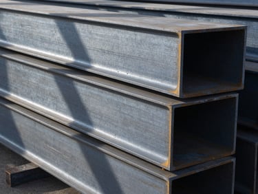 Massive structural steel beams stacked in an industrial warehouse, dramatic shadows, cool metallic tones, sharp details