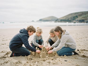 Candid shot of a family building sandcastles on a Cornish beach, natural overcast daylight, soft desaturated tones, 35mm film look.