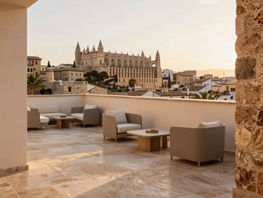 Warm editorial photography of a modern penthouse terrace in Palma de Mallorca, soft golden hour sunlight reflecting on light sandstone tiles, elegant minimalist outdoor furniture, view of historic rooftops, 35mm