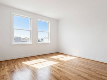 Empty sunlit apartment room with gleaming hardwood floors, white walls, clean windows, sharp focus.
