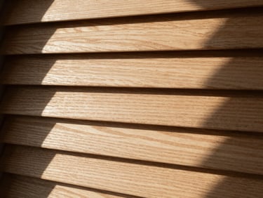 Tactile close-up of custom-stained timber Venetian slats, dramatic directional window light, sharp horizontal shadows, 35mm lens