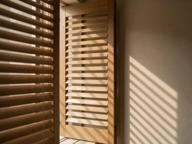 Architectural shutter blinds half-open, casting dramatic diagonal shadow lines on a warm minimalist interior wall, 35mm lens