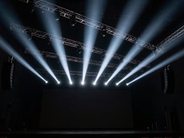 Wide dramatic angle of a modern concert hall stage, complex overhead truss with premium lighting fixtures projecting sharp white beams, high contrast, 35mm