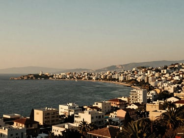 Warm editorial photography of a sweeping wide environmental view of the Athens Riviera coastline at golden hour, low-contrast warm light, medium format film.