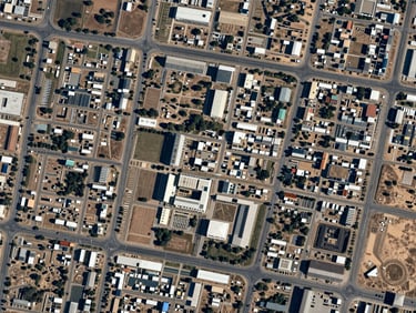 Overhead satellite-style plan view of Dholera SIR development grid, roads and utility corridors visible in geometric precision, project zone highlighted in the central-right quadrant, clean daylight rendering, no people, institutional cartographic clarity