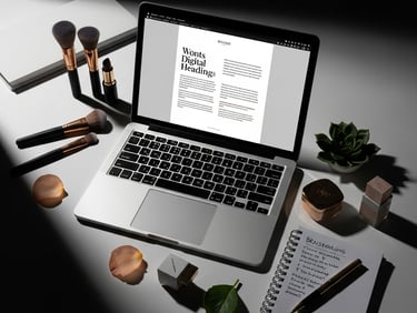 Laptop displaying a digital design document on a desk with makeup brushes and a notebook.