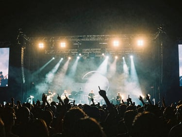 Wide cinematic 16:9 shot of a live music concert with dynamic stage lighting, crowd in silhouette, anamorphic lens flares, deep shadows, 35mm anamorphic lens, cinematic film photography