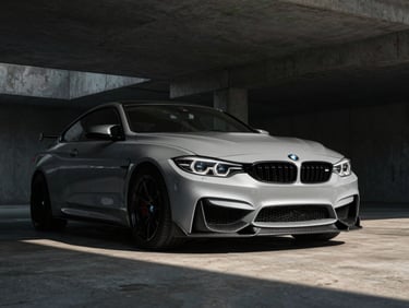 Low-angle front quarter shot of a BMW M4 in a concrete structure, carbon fiber front splitter catching dramatic side-lighting