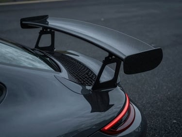 Close-up of a Porsche 911 GT3 rear carbon fiber wing, flawless weave alignment, overcast moody lighting