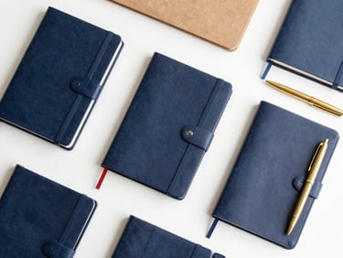 Neatly organized flat-lay of premium stationery, leather-bound journals, elegant brass pens, and minimalist office supplies, soft daylight, 50mm