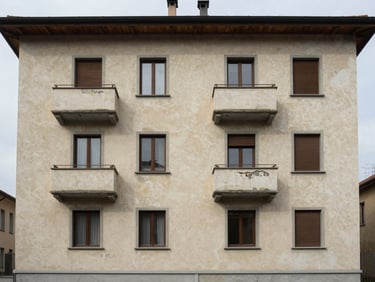 Exterior of a residential apartment building in Northern Italy, freshly painted facade and repaired plasterwork, overcast north light, shot from street level showing the full facade width
