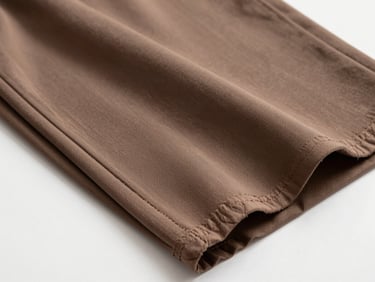 Overhead flat-lay close-up of a folded imported Lycra trouser fabric swatch on a plain white surface, bright even studio lighting, fabric showing slight sheen and stretch-weave structure, no human subject