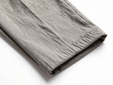 Overhead flat-lay close-up of a folded stretch linen trouser fabric swatch on a plain white surface, bright studio lighting, visible linen yarn texture and open weave detail, no human subject