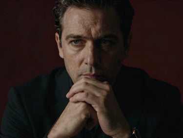 Cinematic close-up portrait of a thoughtful male strategist, hands clasped near chin, low light casting deep shadows, intense focus.