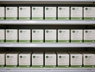 Organized display of edible cannabis product boxes on a retail shelf, straight-on environmental shot, bright clinical retail lighting, clearly printed regulatory labels, no decorative styling