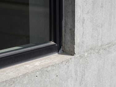 Extreme close-up of a raw concrete wall meeting a minimal black metal window frame, sharp natural light, high-contrast shadows, architectural detail, desaturated tones