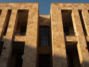Symmetrical low-angle architectural shot of a modern stone facade in Damascus at golden hour, deep shadows, rich gold highlights, elegant editorial photography