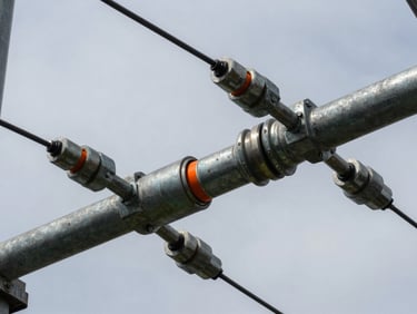 Close-up of high-voltage transmission line hardware, galvanized steel connectors under cool overcast skies.