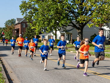 Vibrant action photography of families and kids running down a tree-lined Bath Ohio street during a sunny morning charity fun run, bright natural daylight, 35mm.