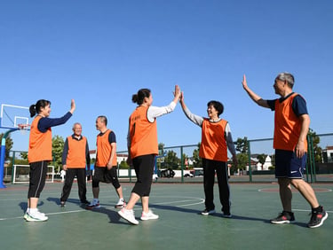 Group of active adults high-fiving on an outdoor basketball court, bright daylight, genuine smiles