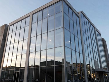 Wide-angle environmental view of a modern cinema glass facade reflecting a bright afternoon sky, clean lines and architectural transparency.