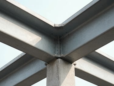 Macro shot of structural steel beams meeting concrete under bright, high-contrast natural daylight, highlighting architectural precision.