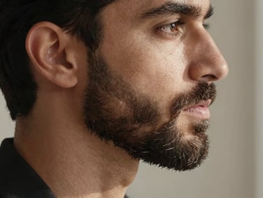 Elegant profile of a refined gentleman with a perfectly groomed, dense beard, warm natural light, soft shadows, clinical luxury aesthetic.