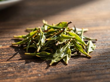 Tight macro detail of tea leaves drying on a dark wood table, soft natural shadows, warm light.