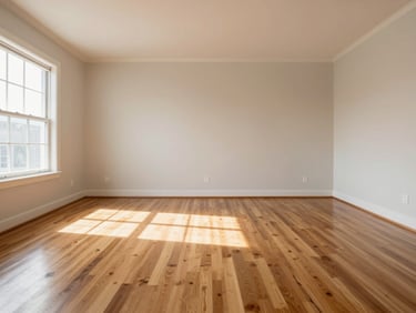 Wide straight-on photograph of a clean residential living room with polished hardwood floors and clear surfaces, bright natural daylight from a window on the left, no occupants, finished state