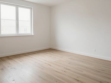Straight-on photograph of a vacant residential flat bedroom with bare floors and freshly wiped skirting boards, bright even daylight from a side window, no furniture, clean state clearly visible