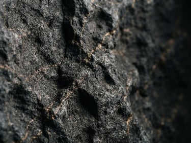 Extreme close-up of dark grey basalt stone with deep cleft textures and subtle gold veining, dramatic low-key architectural side lighting, 35mm