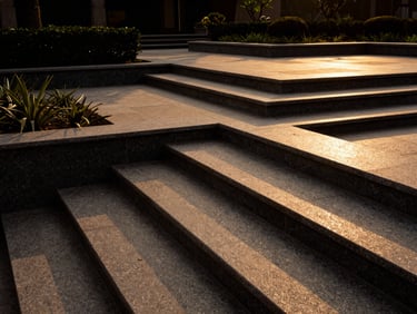 Wide-angle architectural landscape design featuring geometric sandstone steps and dark granite borders, manicured garden setting, dramatic sunset lighting