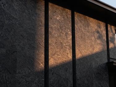 Modern luxury villa facade with dark textured granite wall cladding, sunset side-lighting highlighting the natural cleft finish, architectural photography