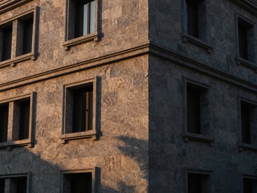 Wide-angle architectural photograph of a luxury residential facade clad in hand-dressed natural grey stone, warm sunset light casting long dramatic shadows, showcasing texture and depth