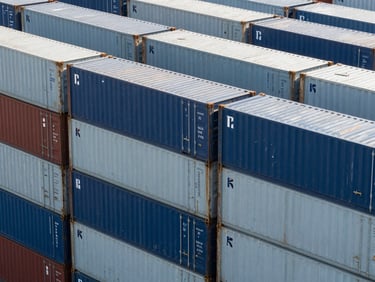High-angle structured pattern of modern shipping containers stacked at a deep-water port, cool crisp daylight, architectural composition