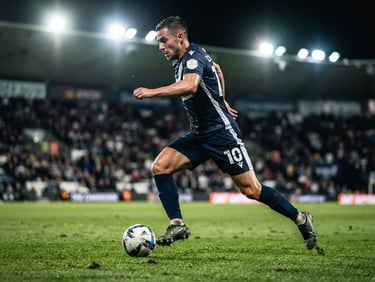 Low-angle dynamic action shot of corporate players in matching kits under dramatic evening stadium floodlights, sharp action freeze-frame, 70-200mm lens.