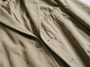 Close-up of fabric weave and stitching on a relaxed tailored jacket, warm diffused natural daylight, soft shadows, macro detail shot, muted earth tones, 35mm film aesthetic