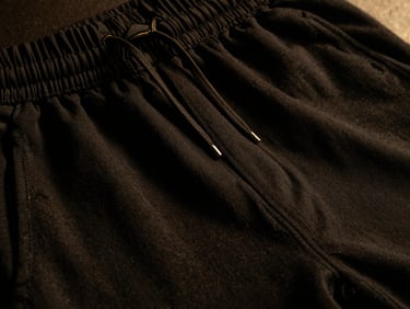 Close-up of a black training jogger fabric, showing texture and subtle gold drawstring detail, low-key lighting.