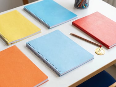 A neat study desk with colorful notebooks, pencils, and a small gold school medal, bright daylight.