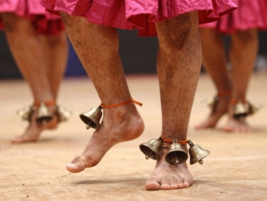 Close-up of ankle bells (ghungroos) tied neatly around a dancer's ankles, warm stage light.