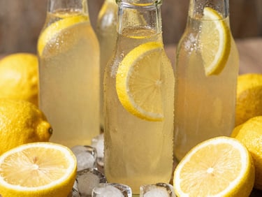 Macro close-up of a chilled glass bottle of lemon tea surrounded by fresh sliced yellow lemons, ice cubes melting under sharp tropical sunlight.