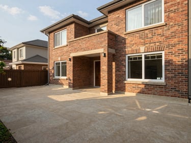 Environmental wide-angle photo of a three-bedroom house backyard showing a covered veranda with exposed brick walls, afternoon light casting soft shadows on the tiled floor, no people, no furnishings